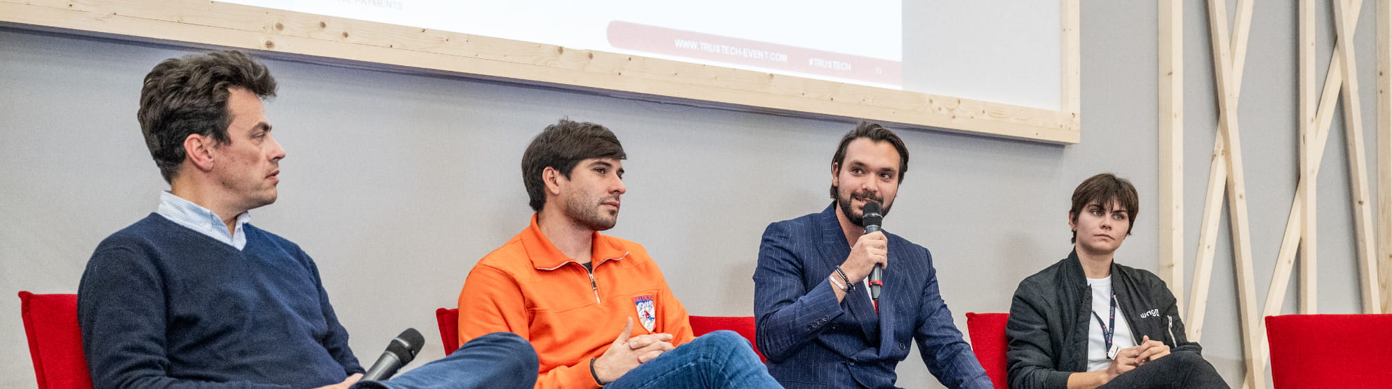 groupe de 4 personnes assises sur scène lors d'une conférence trustech 2023. 3 hommes et une femme. Un homme est entrain d'intervenir un micro à la main. On y voit également le #trustech apparaître