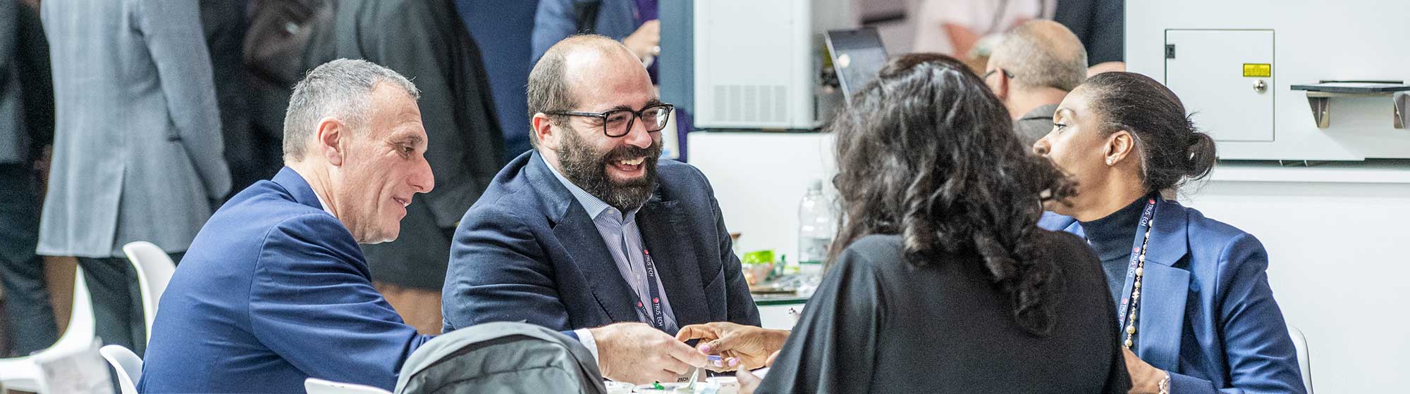 Quatre exposants échangent en souriant autour d'une table sur un stand