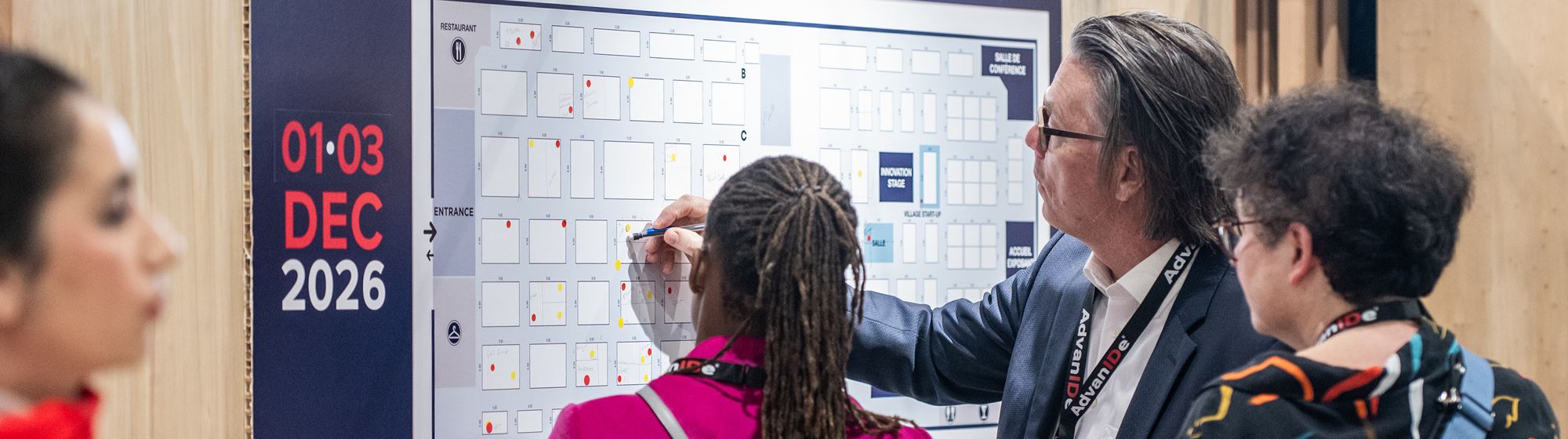 Des exposants consultent un plan du salon avec des couleurs pour identifier les stands disponibles et réservés pour l’édition 2026 de TRUSTECH