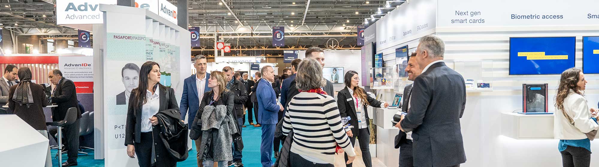 des visiteurs se promenant dans les allees du salon TRUSTECH où on voit aussi des professionnels échanger entre eux sur des stands