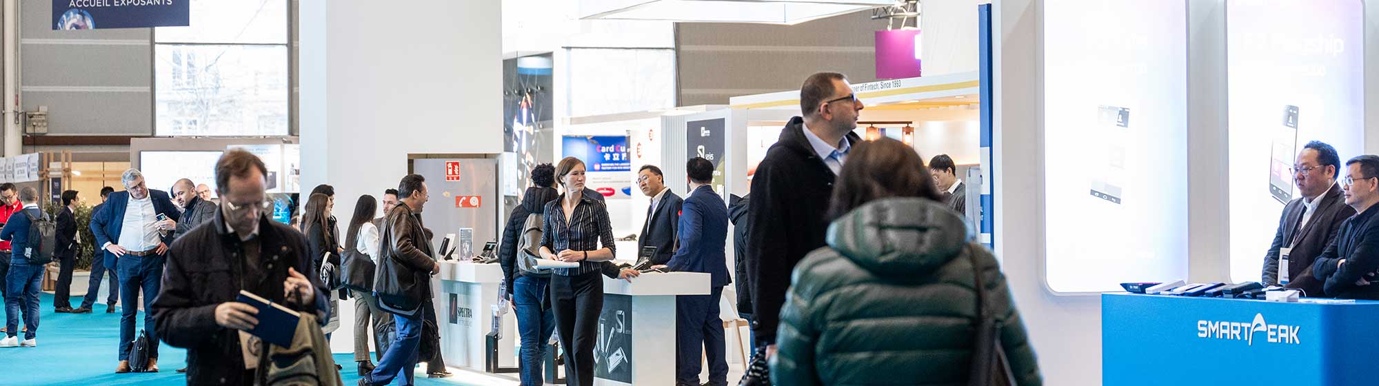 Des visiteurs parcourent les allées du salon trustech en regardant et s'arrêtant sur des stands