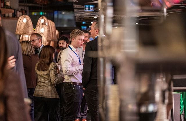 Group of people in a restaurant, suspended lamps illuminate the room, and the atmosphere suggests a social gathering.