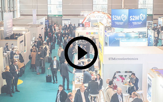 Aerial view of the Trustech exhibition with visitors and booths, with a play icon overlaid.